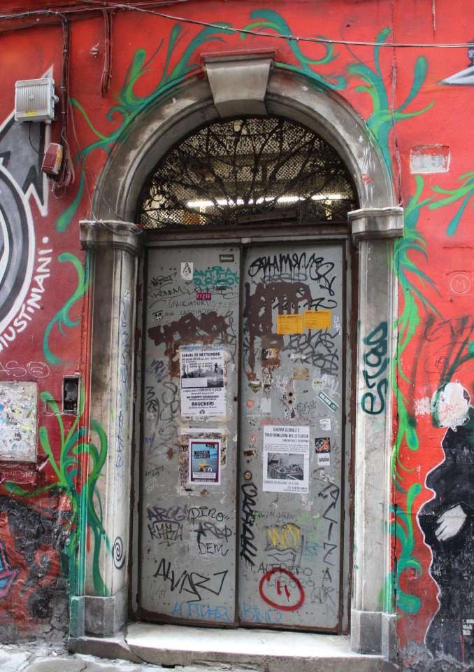 The marble portal on Via dei Giustiniani, with the door covered in graffiti